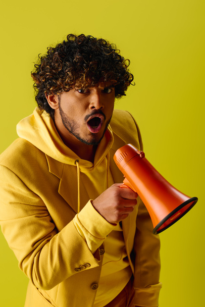 Человек в желтой толстовке держит красный и оранжевый мегафон. - Фото, изображение