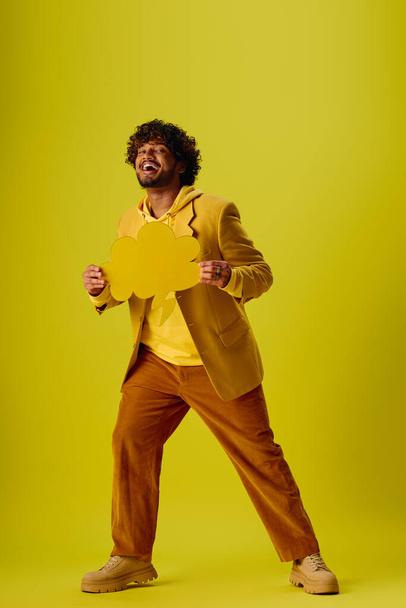 Guapo joven indio en un traje vibrante con confianza sostiene una burbuja de habla amarilla deslumbrante. - Foto, Imagen