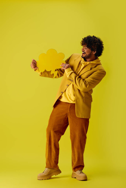 Молодий індійський чоловік у жовтій куртці тримає жовту бульбашку мовлення на яскравому тлі. - Фото, зображення