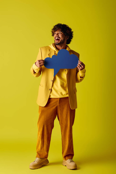 Komea intialainen mies eloisassa keltaisessa puvussa pitää elinvoimaisen sinisen puhekuplan.. - Valokuva, kuva