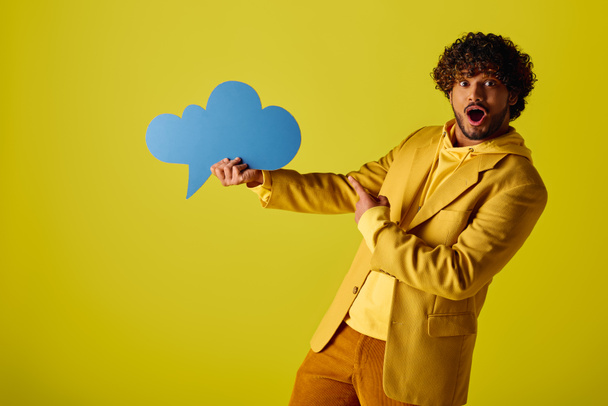 Young Indian man stylishly holds a speech bubble in a vibrant yellow jacket against a colorful backdrop. - Photo, Image