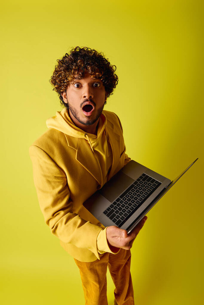 Handsome young Indian man with curly hair holding a laptop on vibrant backdrop. - Photo, Image