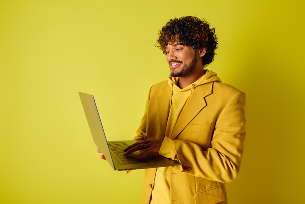 Egy jóképű, fiatal indiai férfi élénk sárga öltönyben, laptoppal a kezében.. - Fotó, kép