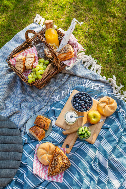 Picnic edredón y cesta con diferentes alimentos, frutas, zumo de naranja., yogur y pan sobre hierba verde - Foto, Imagen