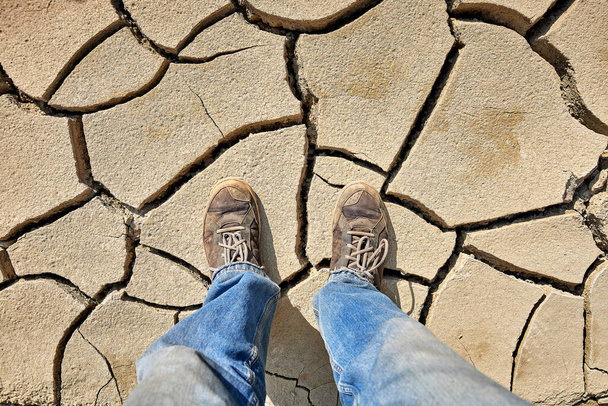 vista superior de las piernas del hombre de pie sobre tierra agrietada en el desierto - Foto, imagen