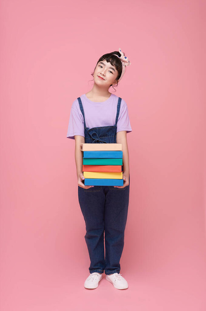 young Asian girl or elementary school girl holding books isolated on pink background. - Photo, Image