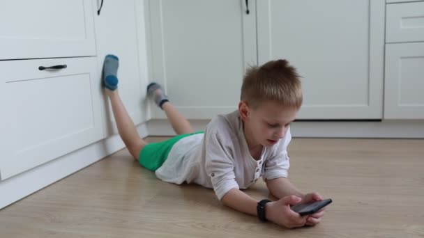 Yerde yatan ve cep telefonuna sarılmış genç bir çocuk görülüyor. Cihazı tıklar ve siler, içeriği kaydırır. Çocuk odaklanmış ve dijital aktivitesine dalmış gibi görünüyor.. - Video, Çekim