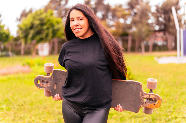 Fröhlich lächelnde junge Frau mit Skateboard im Park - Foto, Bild