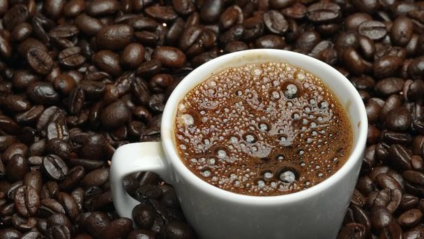 Закрыть пузырек ароматного горячего кофе в чашку с черным фоном. Горячий кофе или эспрессо наливается в белый кофе чашки падают в кипяченую воду с разделенным черным фоном. Comestible. - Фото, изображение