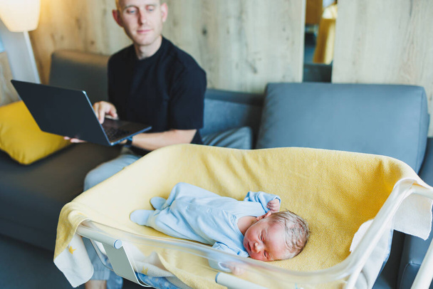 Houden van jonge vader die aan laptop werkt en naast de baby zit. Thuis werken met een klein kind - Foto, afbeelding