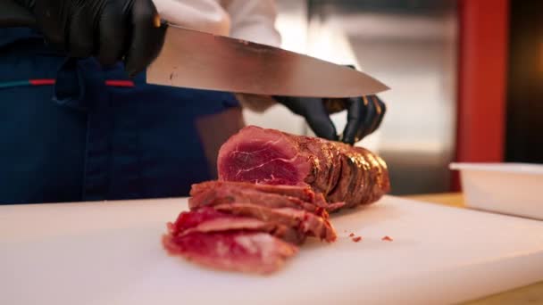 close-up van een chef-kok handen in zwarte handschoenen snijden van een stuk rauw vlees op een plank - Video