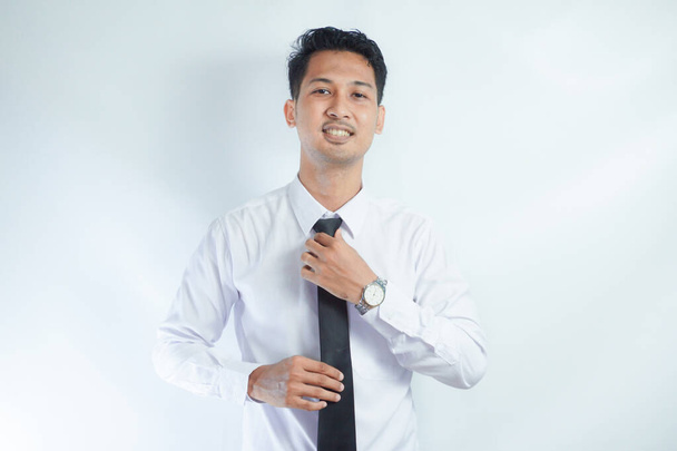 Hombre de negocios guapo enderezando su corbata sobre fondo blanco y mirando a la cámara - Foto, imagen