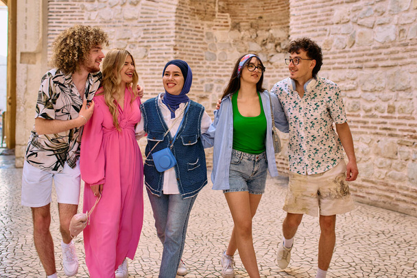 Různorodá skupina turistů, oblečená v letních šatech, se prochází turistickým městem se širokými úsměvy a vychutnává si jejich vyhlídkové dobrodružství.  - Fotografie, Obrázek