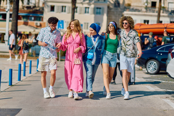 Een gevarieerde groep toeristen, gekleed in zomerkleding, slentert door de toeristische stad met brede glimlachen, genietend van hun sightseeing avontuur.  - Foto, afbeelding