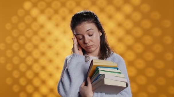 Vrouw met bezorgde gezichtsuitdrukking die migraine pijn voelt, boeken bij zich draagt voor schoolexamen, studioachtergrond. Gestresste student met leerboeken die hoofdpijn hebben van te veel huiswerk, camera B - Video