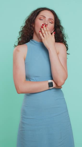 Tired exhausted young Caucasian woman yawning, sleepy inattentive feeling somnolent lazy bored gaping suffering from lack of sleep, insomnia. Girl isolated on blue studio background indoors. Vertical - Footage, Video