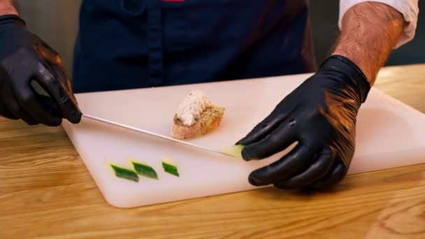 Close-up van de handen het plaatsen van komkommer plakjes op een sandwich in een professionele keuken - Video