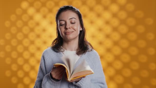 Portrait de femme souriante tenant des pages odorantes de livre transmettant la joie du concept de lecture, arrière-plan de studio. Gai personne qui aime nouveau roman odeur fraîche, montrant béatitude, caméra B - Séquence, vidéo