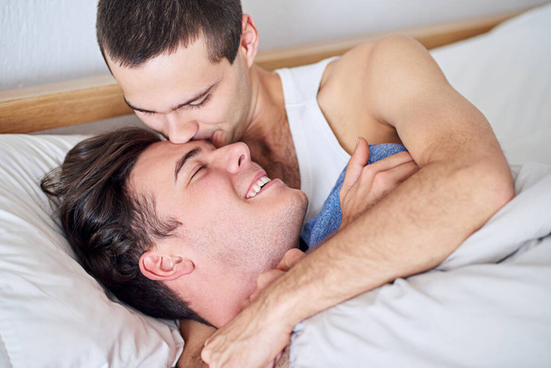 Onnellinen, homo pari ja sänky suudelma rentoutua rakkautta, hoitoa tai hellyyttä yhdessä kotona. LGBTQ tai mies henkilö hymyillä tai halata romantiikkaa, läheisyyttä tai ystäville nauttia loma viikonloppuna makuuhuoneessa. - Valokuva, kuva