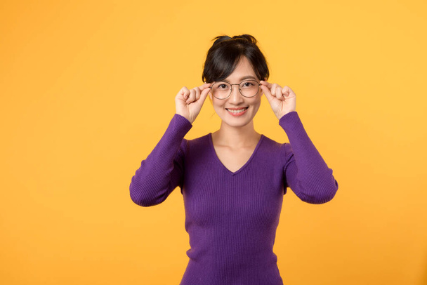 Retrato de jovem mulher asiática vestindo camisa roxa, trabalhador da empresa em óculos, sorrindo, de pé sobre fundo amarelo - Foto, Imagem