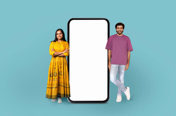 Indyjska kobieta w tradycyjnej sukience i mężczyzna w swobodnym ubraniu stoją obok dużego pustego ekranu smartfona, sugerując zastosowanie technologii - Zdjęcie, obraz