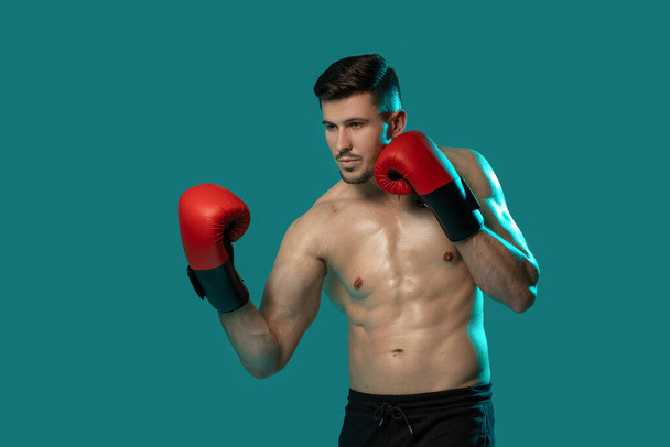 Ein muskulöser Mann steht hemdlos mit Boxhandschuhen bereit für Training oder Sparring. Seine Haltung deutet auf Konzentration und Entschlossenheit hin und deutet auf einen bevorstehenden Boxkampf oder eine Trainingseinheit hin.. - Foto, Bild
