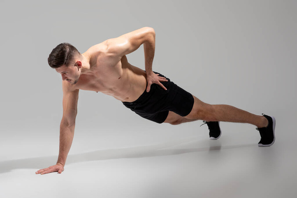 Mężczyzna balansuje na jednej ręce podczas wykonywania pompki, angażując swój rdzeń, klatkę piersiową i tricepsy w wymagającym ćwiczeniu dla siły i stabilności. - Zdjęcie, obraz