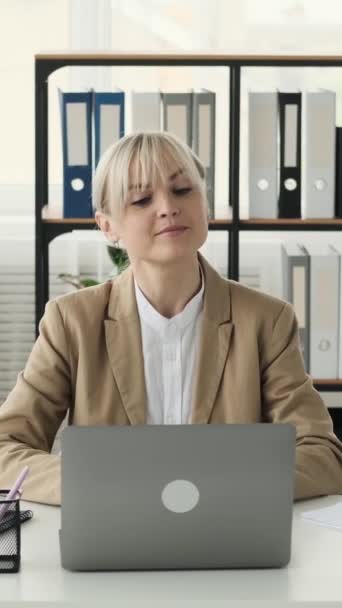 Poważny profesjonalny biały kobieta freelancer zaangażowany w papierkowej pracy i rozmowy wideo z laptopem podczas pracy w biurze. Koncepcja komunikacji online. Pionowe wideo. - Materiał filmowy, wideo