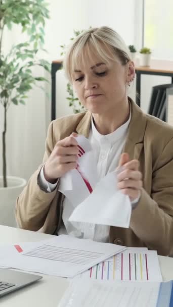 Boze en agressieve blanke zakenvrouw scheurt documenten terwijl ze op kantoor werkt. Emotionele stress en mislukking concept. Verticale video. - Video