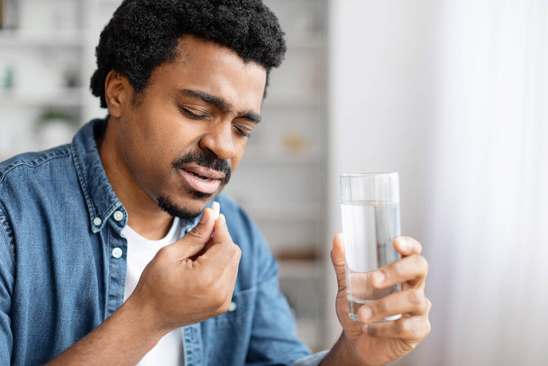 Hombre afroamericano en casa a punto de tomar medicamentos, sugiriendo atención médica o rutina de bienestar, espacio para copiar - Foto, imagen