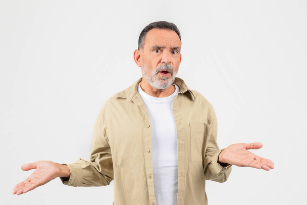 A senior man is standing with his hands extended out in front of him. He appears to be confused or shocked by something, white background - Photo, Image
