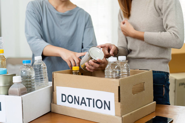 dobroczynność, darowizna i wolontariat. Wolontariuszka przygotowuje pudełko z żywnością dla biednych, ofiar katastrof w domu.. - Zdjęcie, obraz