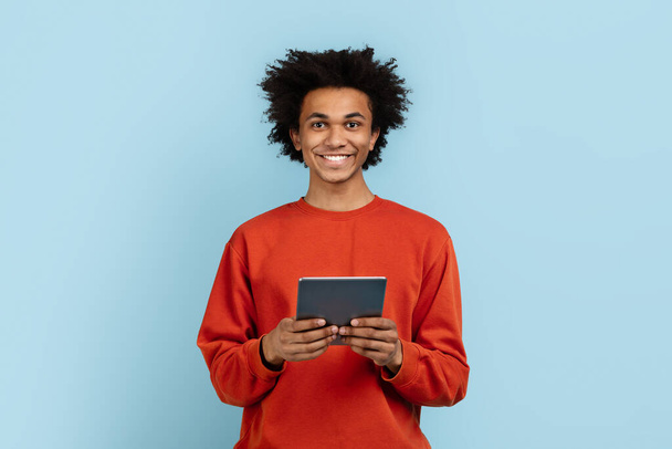 青い背景に隔離されたデジタルタブレットを保持しているカジュアルなアフリカ系アメリカ人男性は,利便性と使いやすさを示唆しています - 写真・画像