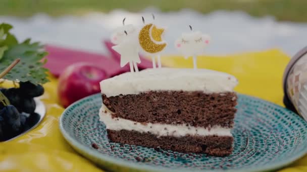 Detailní pohled na rozkošný plátek dortu zdobený kreativními svršky, uspořádaný na stylovém talíři na venkovním shromáždění. Detailní záběr lahodného dortu na venkovní piknikové párty - Záběry, video