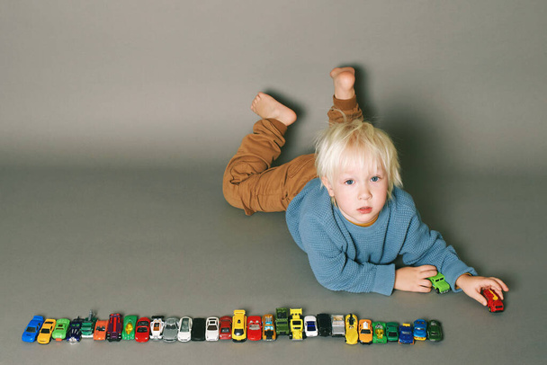 Estúdio retrato no fundo cinza de adorável menino brincando com muitos carros de brinquedo - Foto, Imagem