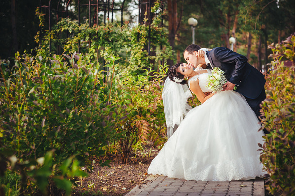 Young couple kissing in wedding gown. Bride holding bouquet of flowers - Foto, Imagen