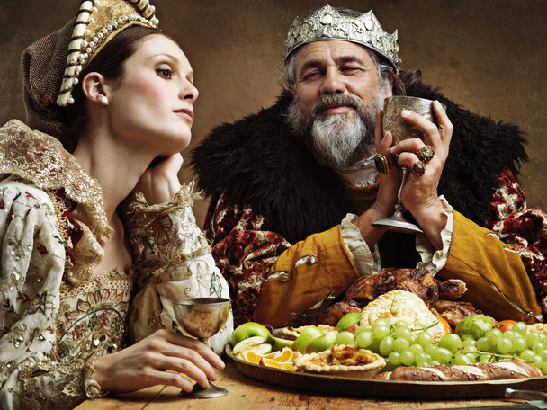 Koning, koningin en feest met wijn aan tafel voor een heerlijk diner in koninklijk banket, vintage en majestueus met kroon. Monarch, echtgenoot en verveeld samen met alcohol en buffet voor formele viering. - Foto, afbeelding