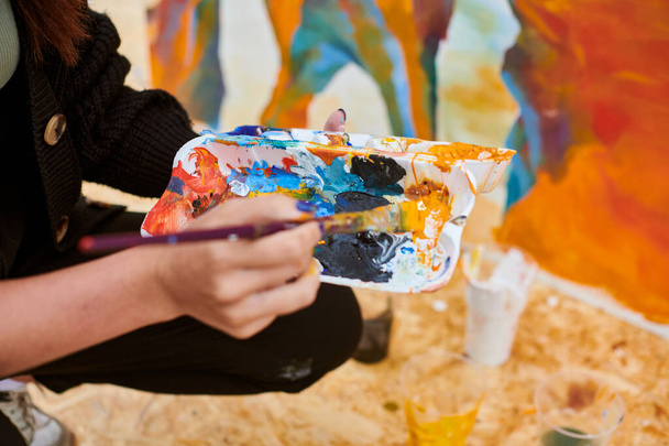 Жіноча рука художника занурює пензлик в палітру барвистих фарб для живої картини зображення для виставки на вулиці, крупним планом, рука художника, що тримає пензлик - Фото, зображення