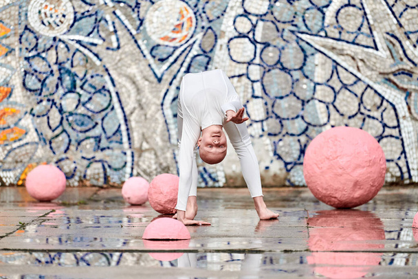Baile al aire libre de la joven bailarina con alopecia en traje futurista blanco con movimientos plásticos y flexibles entre esferas rosadas sobre fondo abstracto mosaico soviético, simboliza la autoexpresión - Foto, imagen