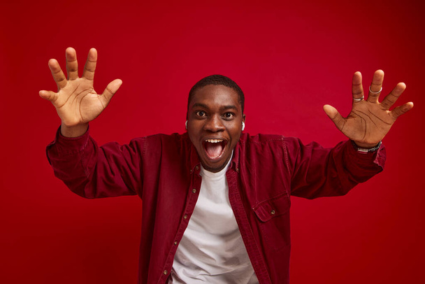 молодий афроамериканський чоловік радіє з руками до камери, ізольований на червоному фоні студійний портрет - Фото, зображення