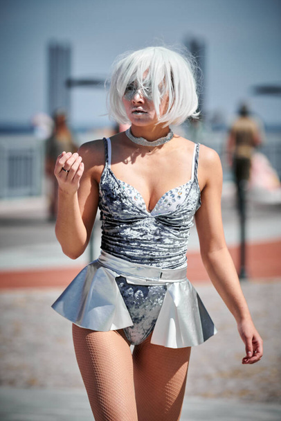 Young sexy girl in space silver micro skirt dancing with smooth, feminine and graceful movements, female outdoor dance performance on seaside promenade creating an arousing outdoor spectacle - Photo, Image