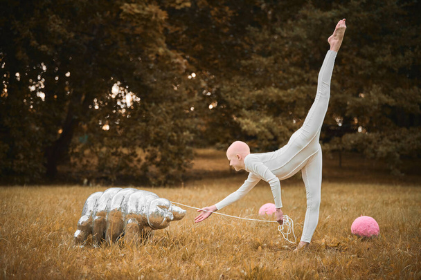 Porträt eines jungen haarlosen Mädchens Ballerina mit Alopezie in weißem Tuch spielen mit tegradiertem Spielzeug im Herbst Park, surreale Szene mit glatzköpfigen Teenager-Mädchen reflektieren miteinander verflochtene Fäden des Lebens und der Kunst - Foto, Bild