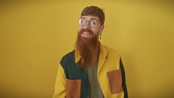 Cheerful young redhead man, grinning ear-to-ear, sporting glasses and a shirt, standing over an isolated yellow background. flaunting a victory sign, he's a symbol of success! - Footage, Video