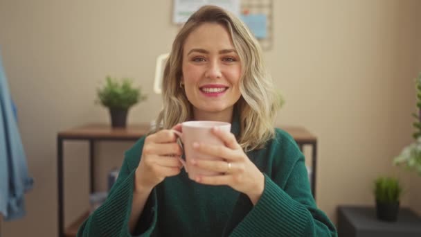 Uma jovem mulher sorrindo desfruta de um momento acolhedor dentro de casa, segurando uma xícara em uma sala de estar bem decorada. - Filmagem, Vídeo