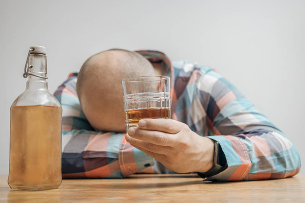 Verslaafde en dronken man aan tafel met een glas alcohol, whisky of cognac, alcoholisme en slechte gewoonten concept. - Foto, afbeelding