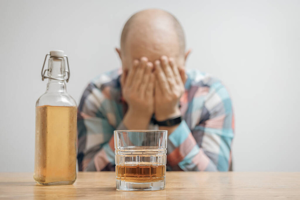 Εθισμένος και μεθυσμένος άνθρωπος στο τραπέζι με ένα ποτήρι αλκοόλ ποτό, ουίσκι ή μπράντι, αλκοολισμός και κακές συνήθειες έννοια. - Φωτογραφία, εικόνα