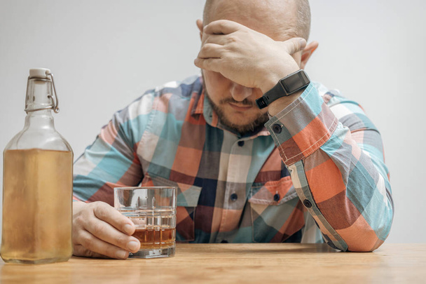 Εθισμένος και μεθυσμένος άνθρωπος στο τραπέζι με ένα ποτήρι αλκοόλ ποτό, ουίσκι ή μπράντι, αλκοολισμός και κακές συνήθειες έννοια. - Φωτογραφία, εικόνα