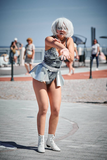 Joven chica sexy en el espacio micro falda de plata bailando con movimientos suaves, femeninos y elegantes, actuación de danza al aire libre femenina en el paseo marítimo creando un espectáculo al aire libre excitante - Foto, imagen