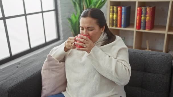 Una donna matura rilassata gode di una bevanda calda nel suo accogliente soggiorno, impregnando un senso di comfort e stile di vita. - Filmati, video