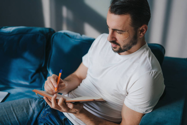 Un homme caucasien écrit des pensées dans son journal. Créatif prenant des notes dans un bloc-notes. - Photo, image